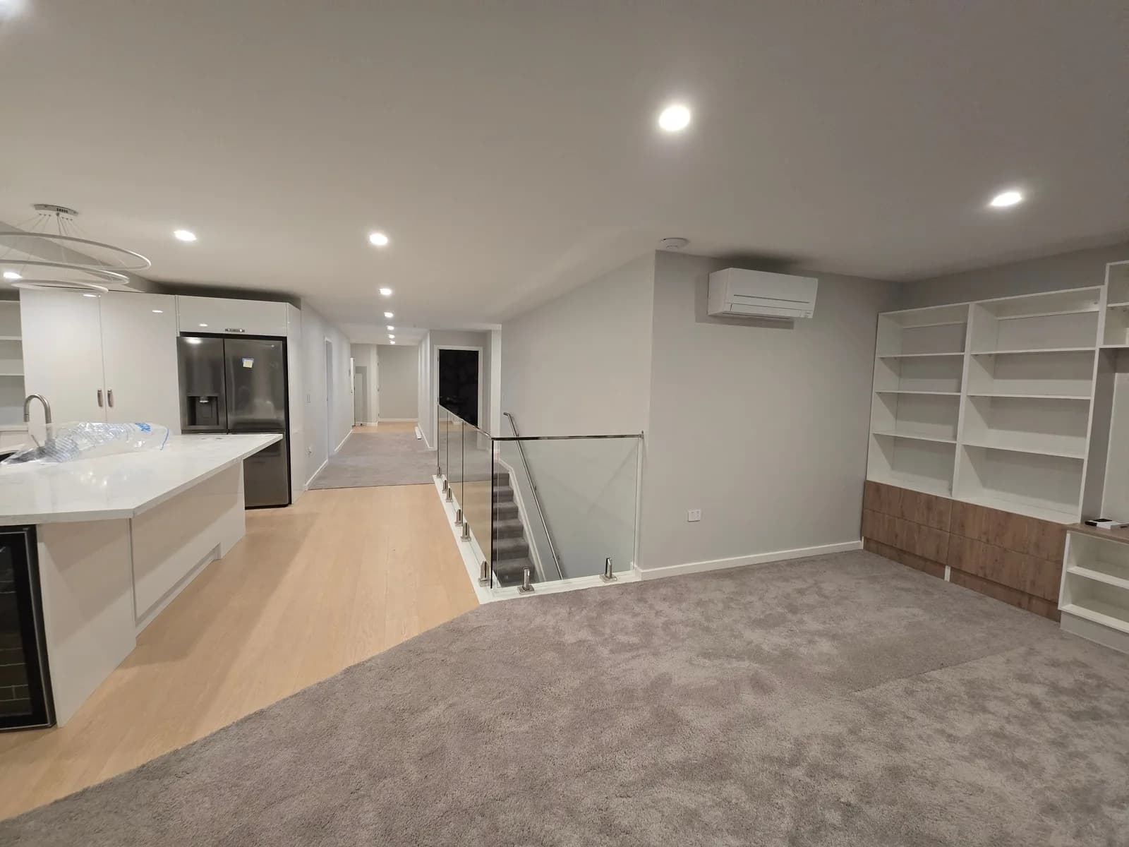 Open-plan upstairs living area with white walls and ceiling, a kitchen island, built-in shelving and a glass stair balustrade