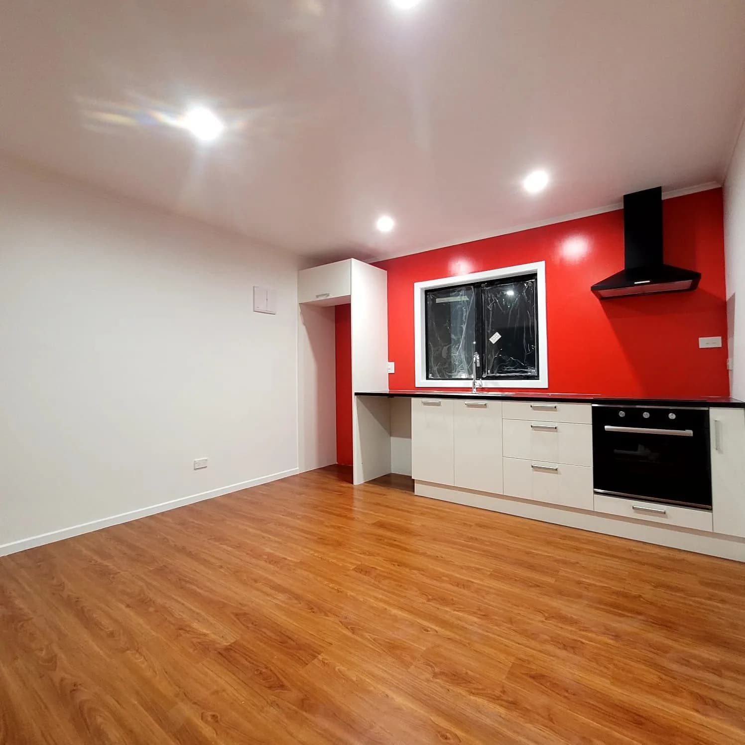 Finished kitchen with a red feature wall, white cabinetry, white ceiling and timber floor