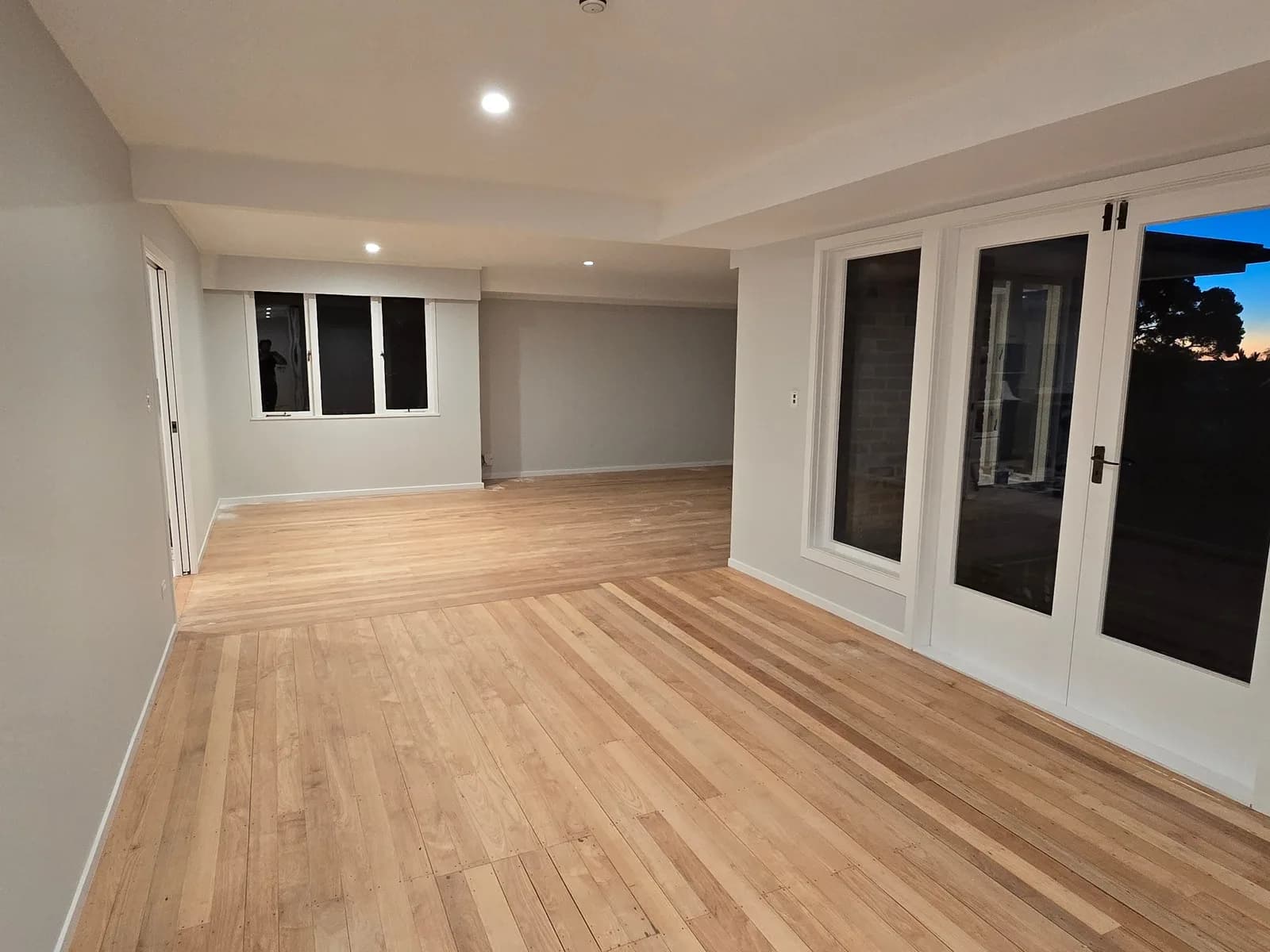 Large empty room painted white with French doors and a new oak floor in afternoon sun