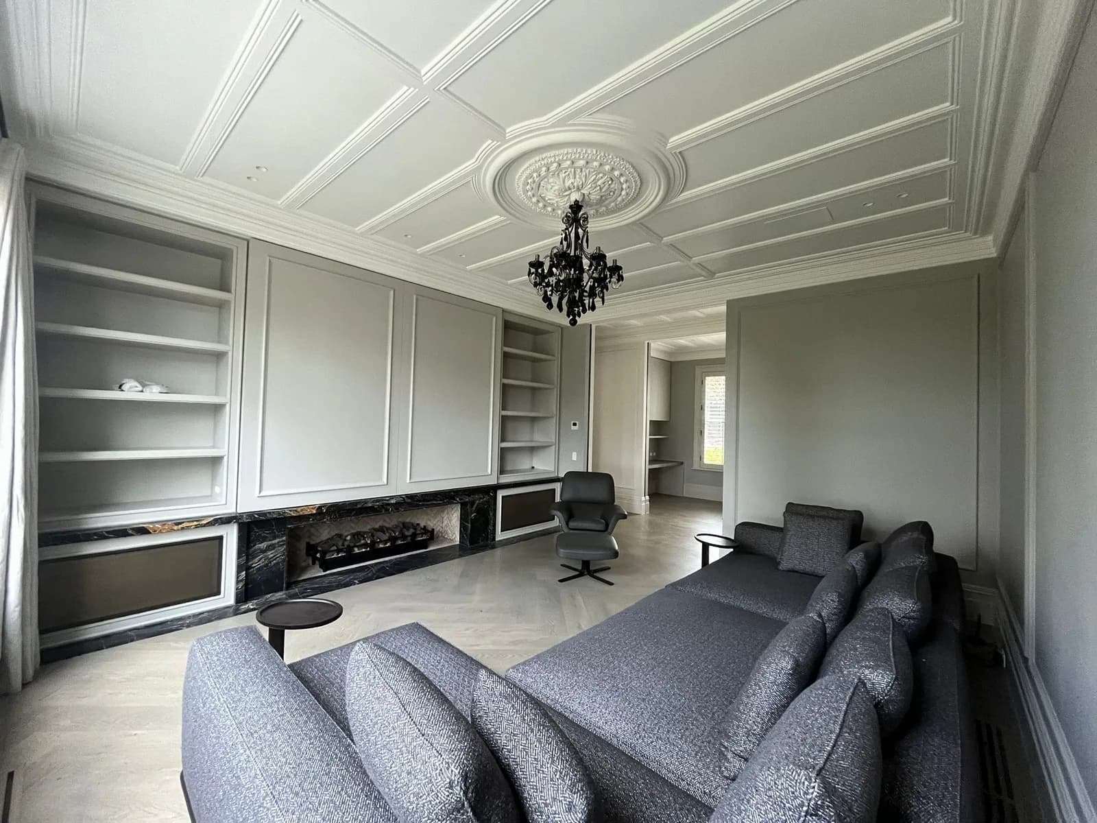 Living room with painted built-in shelving, panelled walls, a coffered white ceiling and a black chandelier