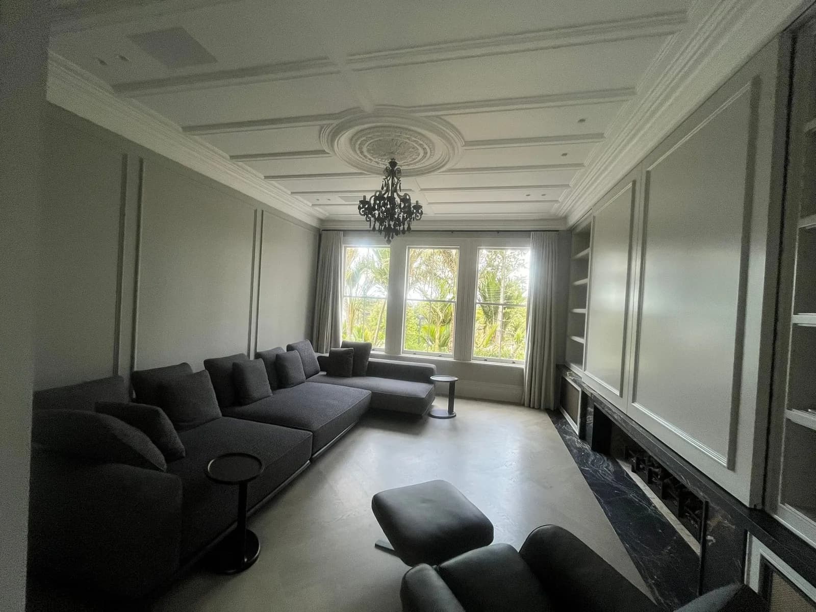 Villa lounge with panelled walls and ceiling painted in pale grey, a ceiling rose with a black chandelier and a grey sectional sofa