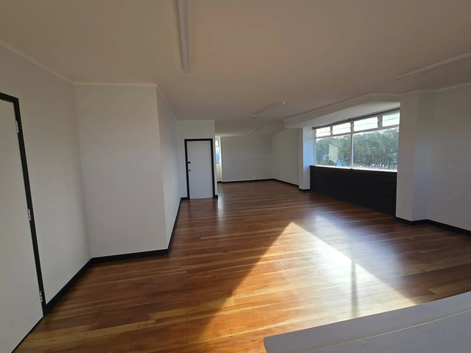 Empty room painted white with a polished timber floor and sun through the window